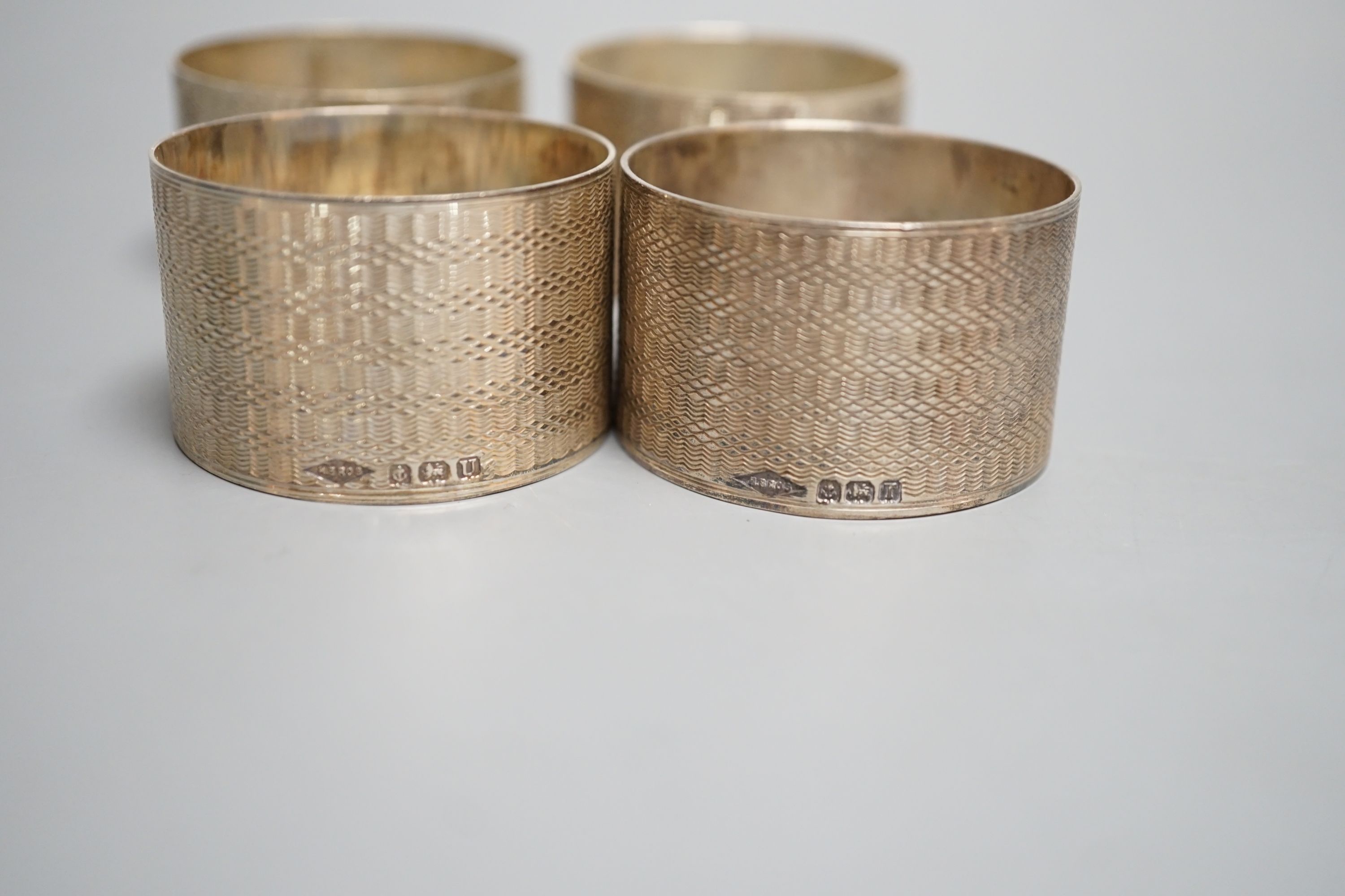 A set of four George VI engine turned silver napkin rings, H. Bros, Birmingham, 1943/4, two engraved with names.